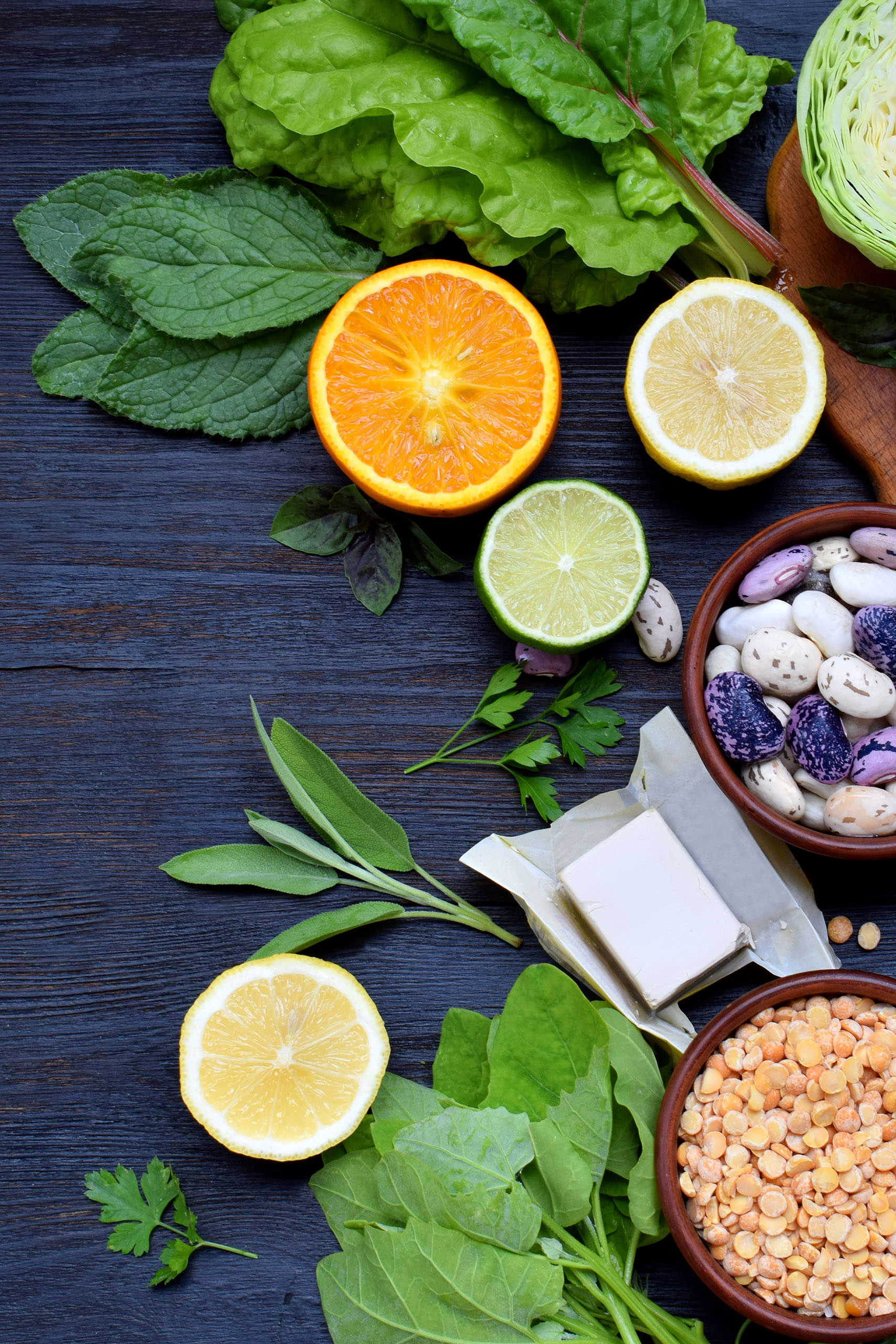 Composition on a dark background of products containing folic acid, vitamin B9 – green leafy vegetables, citrus, beans, peas, nuts, yeast. Top view. Flat lay